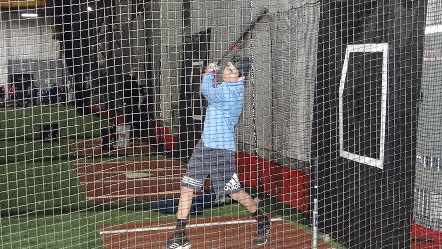 A player taking swings in one of the batting cages